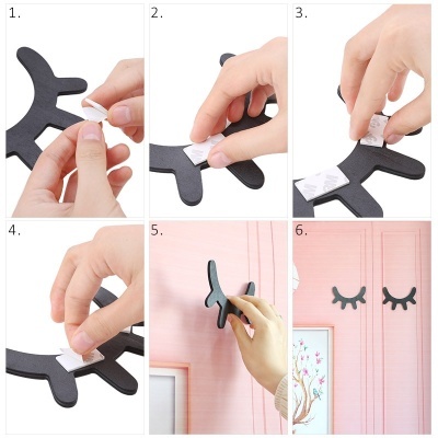 Mãos a aplicar autocolantes de pestanas pretas na parede cor-de-rosa