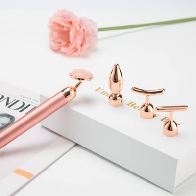 Massageador facial elétrico rosa com cabeças intercambiáveis e flor rosa ao fundo