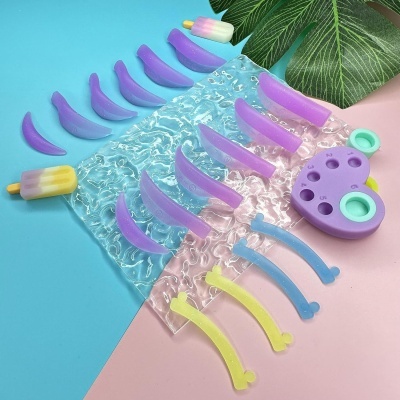 Acessórios coloridos de plástico organizados sobre um saco plástico texturizado com fundo azul e rosa.