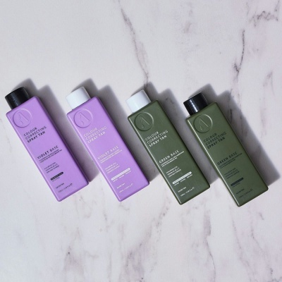 Frascos de spray corrector de cor violet e green base com tampas preta e branca sobre fundo branco marmoreado.
