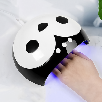 Aparelho secador de unhas branco e preto em formato de panda com luz azul em uso