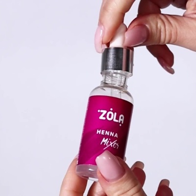 Frasco pequeno com rótulo roxo e texto branco ZOLA Henna Mix, segurado por mãos femininas com unhas rosa claro.