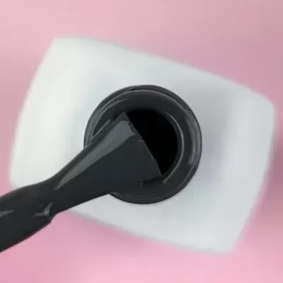 Pincel de verniz preto dentro de frasco branco sobre fundo rosa