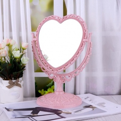 Espelho de mesa rosa em forma de coração com moldura decorativa e flores artificiais ao lado