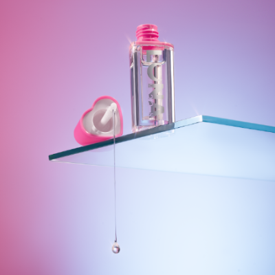 Frasco transparente de verniz para unhas com tampa rosa aberta em forma de coração e gota de verniz escorrendo.