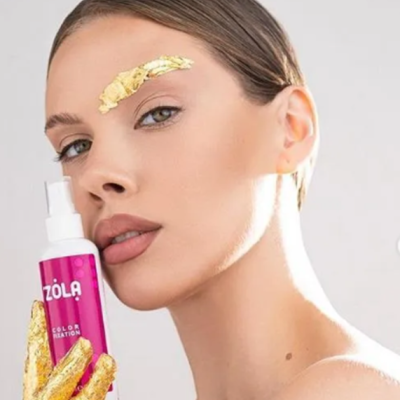 Mulher com folhas douradas na pele segurando spray ZOLA COLOR REATION