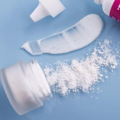 Frasco de creme branco, pó branco e embalagem tubular branca e rosa sobre fundo azul