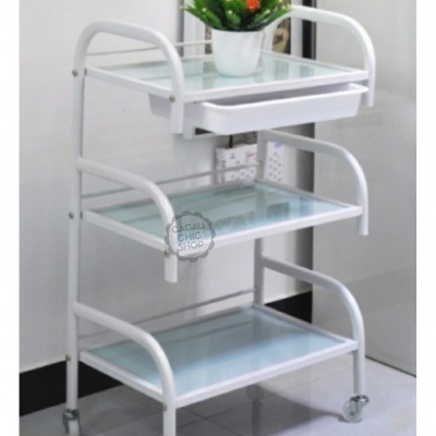 Carrinho branco com prateleiras de vidro, gaveta e vaso de flores laranja em ambiente interior