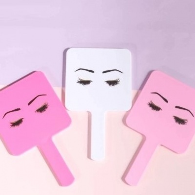Três espelhos de mão com sobrancelhas e pestanas desenhadas, em cores rosa e branco