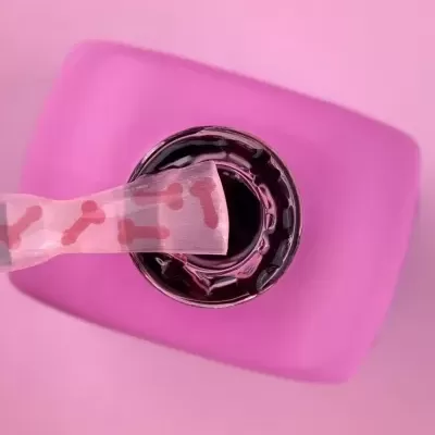 Garrafa com líquido escuro e tampa roxa com adesivo de ossos cor-de-rosa.