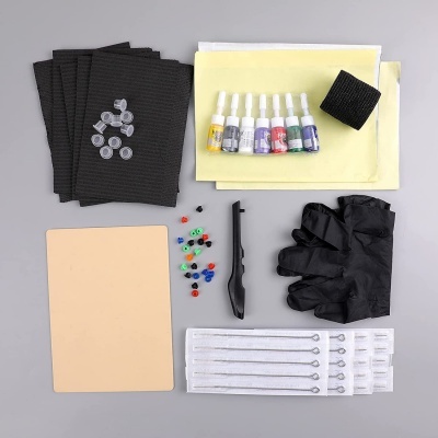 Kit de tatuagem com luvas, tintas coloridas, agulhas e outros acessórios em fundo cinzento