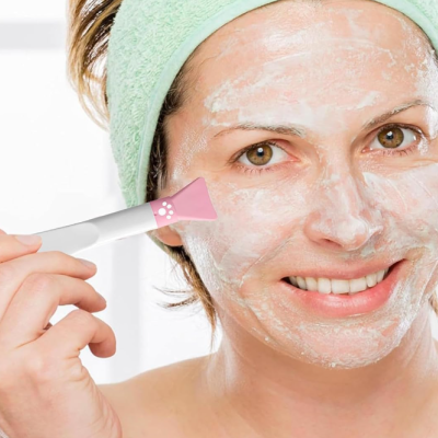 Mulher a aplicar máscara facial branca com aplicador rosa e branco