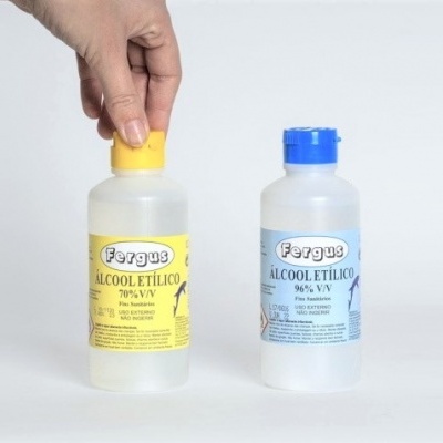 Duas garrafas plásticas de álcool etílico Fergus com rótulos amarelo e azul e tampas coloridas, uma segurada por uma mão.
