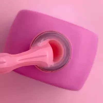 Frasco rosa aberto com espátula plástica cor-de-rosa sobre fundo rosa