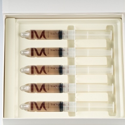 Cinco seringas com líquido castanho organizadas numa caixa branca.