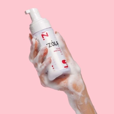 Mão com espuma a segurar frasco branco de produto ZOLA