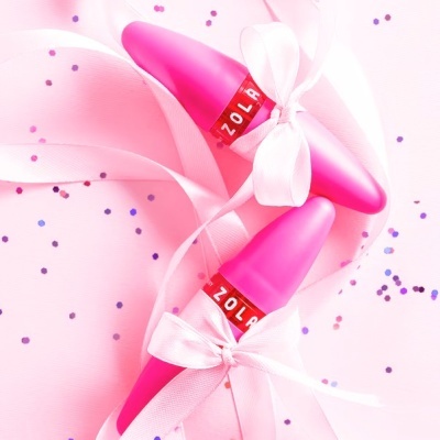 Dois produtos cor-de-rosa com laços brancos e faixa vermelha ZOLA sobre fundo cor-de-rosa com glitter