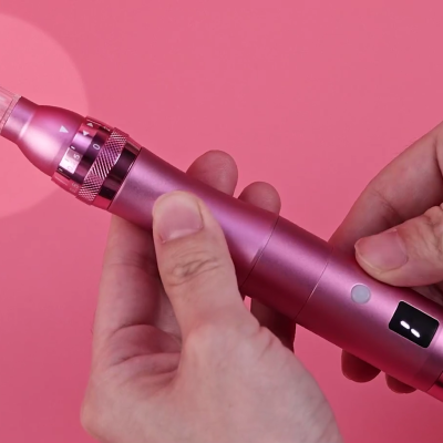 Dispositivo elétrico portátil rosa com visor digital e botão, segurado por mãos sobre fundo rosa