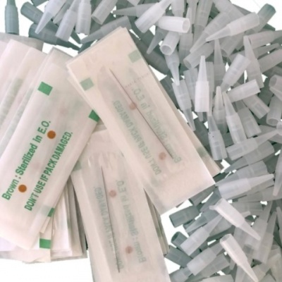 Agulhas descartáveis em embalagens transparentes com texto verde e laranja, com várias agulhas soltas ao fundo