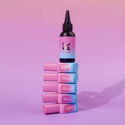 Conjunto de frascos de verniz rosa e azul, empilhados com rótulos visíveis e fundo rosa suave.