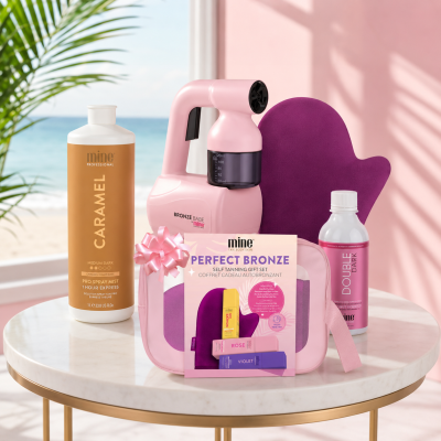 Conjunto de autobrônzeador com spray, aparelho, luva, embalagem de presente, frasco e bolsa em cenário de praia e parede rosa.
