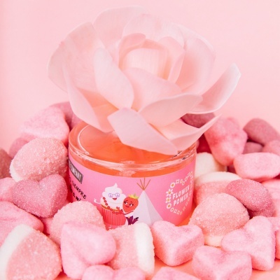 Frasco rosa com creme e flor artificial rodeado por doces cor-de-rosa e branco.