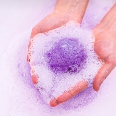 Mãos com espuma branca e bolha roxa em fundo roxo claro