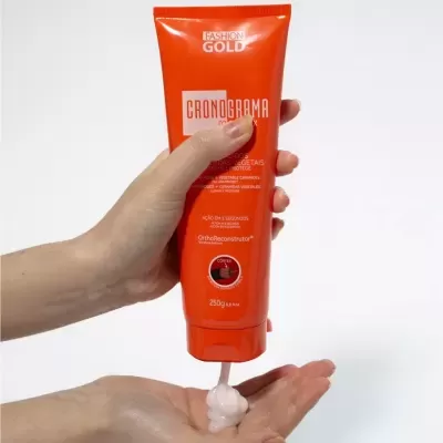 Frasco laranja de creme Cronograma Capilatis Gold com creme a ser colocado na mão