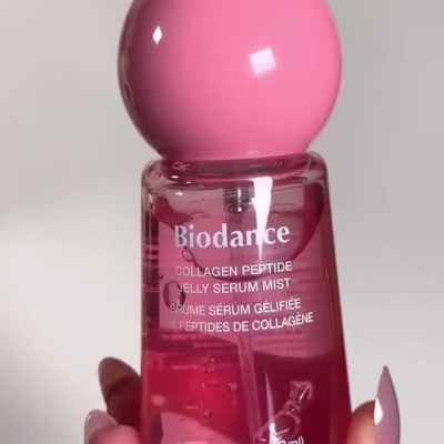 Frasco rosa translúcido de sérum Biodance com tampa esférica cor-de-rosa a ser manuseado e aplicado na pele