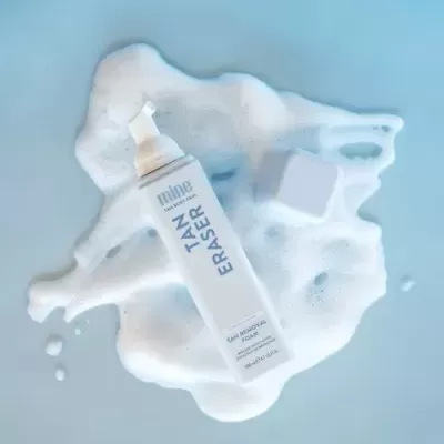 Frasco branco de espumador com texto TAN ERASER sobre espuma branca em fundo azul