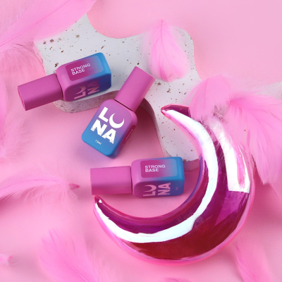 Frascos de verniz LUNA Strong Base sobre superfície com penas cor-de-rosa e lua decorativa