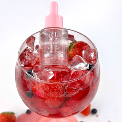 Frasco com conta-gotas rosa sobre gelo e frutos vermelhos num copo de vidro