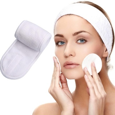 Mulher com faixa branca e disco de algodão ao lado de luva esfoliante branca