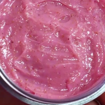 Frasco de cosmético rosa cremoso com textura demonstrada no dedo.