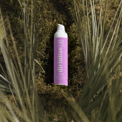 Frasco de produto cosmético cor-de-rosa sobre musgo verde com folhas ao redor