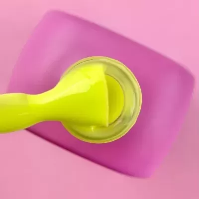 Frasco aberto de verniz amarelo com pincel sobre superfície rosa e base roxa