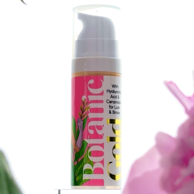 Frasco de produto cosmético Botanic Gold com doseador em fundo branco e flores desfocadas