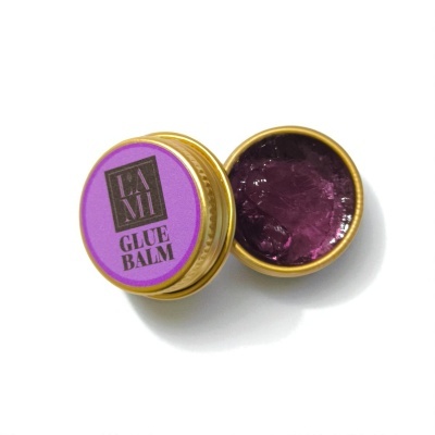 Recipiente dourado aberto com gel roxo e tampa roxa com texto LASH GLUE BALM
