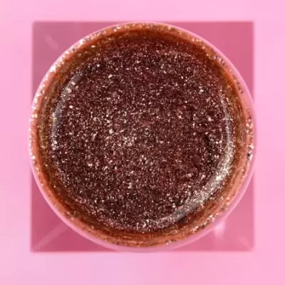 Frasco de vidro com produto granuloso castanho visto de cima sobre fundo rosa