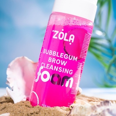 Frasco de espuma rosa para limpeza de sobrancelhas ZOLA na areia junto a conchas
