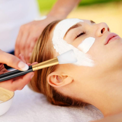 Pincel aplicador de máscara facial aplicando creme branco no rosto de uma mulher