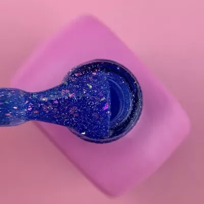 Frasco de verniz de unhas azul com glitter colorido sobre fundo rosa.