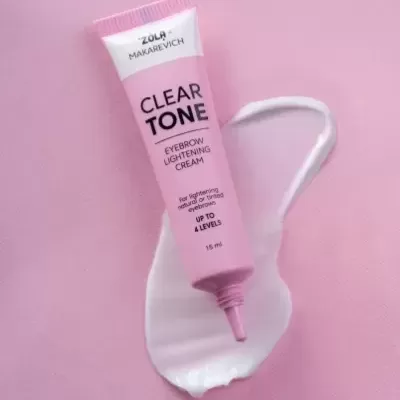 Tubo rosa de creme para clarear sobrancelhas sobre fundo rosa com creme branco
