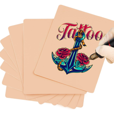 Conjunto de cadernos com capa cor de pele e desenho colorido de âncora com rosas e a palavra 'Tattoo' sendo desenhada por mão com luva