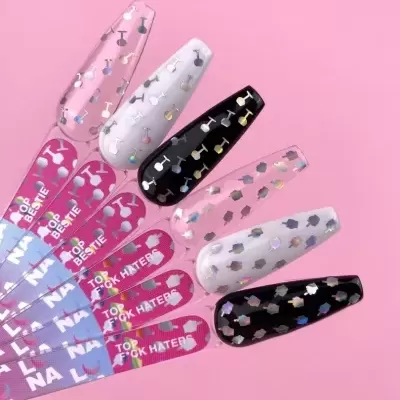 Amostras de unhas artificiais com padrões holográficos e fitas adesivas rosa com texto.