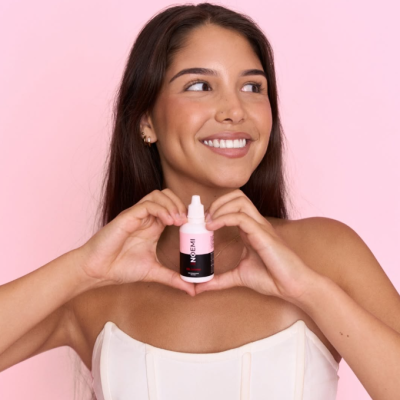 Mulher jovem segurando frasco branco e rosa com rótulo 'NO FERI'