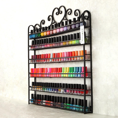 Expositor metálico preto com vernizes de unhas variados e organizados por cores numa parede clara.