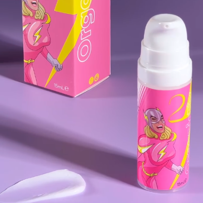 Frasco e embalagem rosa com ilustração de super-heroína e creme branco sobre superfície lilás