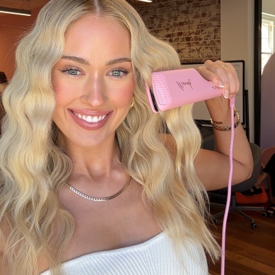 Mulher com cabelo loiro ondulado usando alisador de cabelo rosa