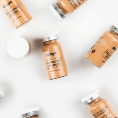 Frascos pequenos de vidro com líquido castanho claro e tampas brancas sobre fundo branco